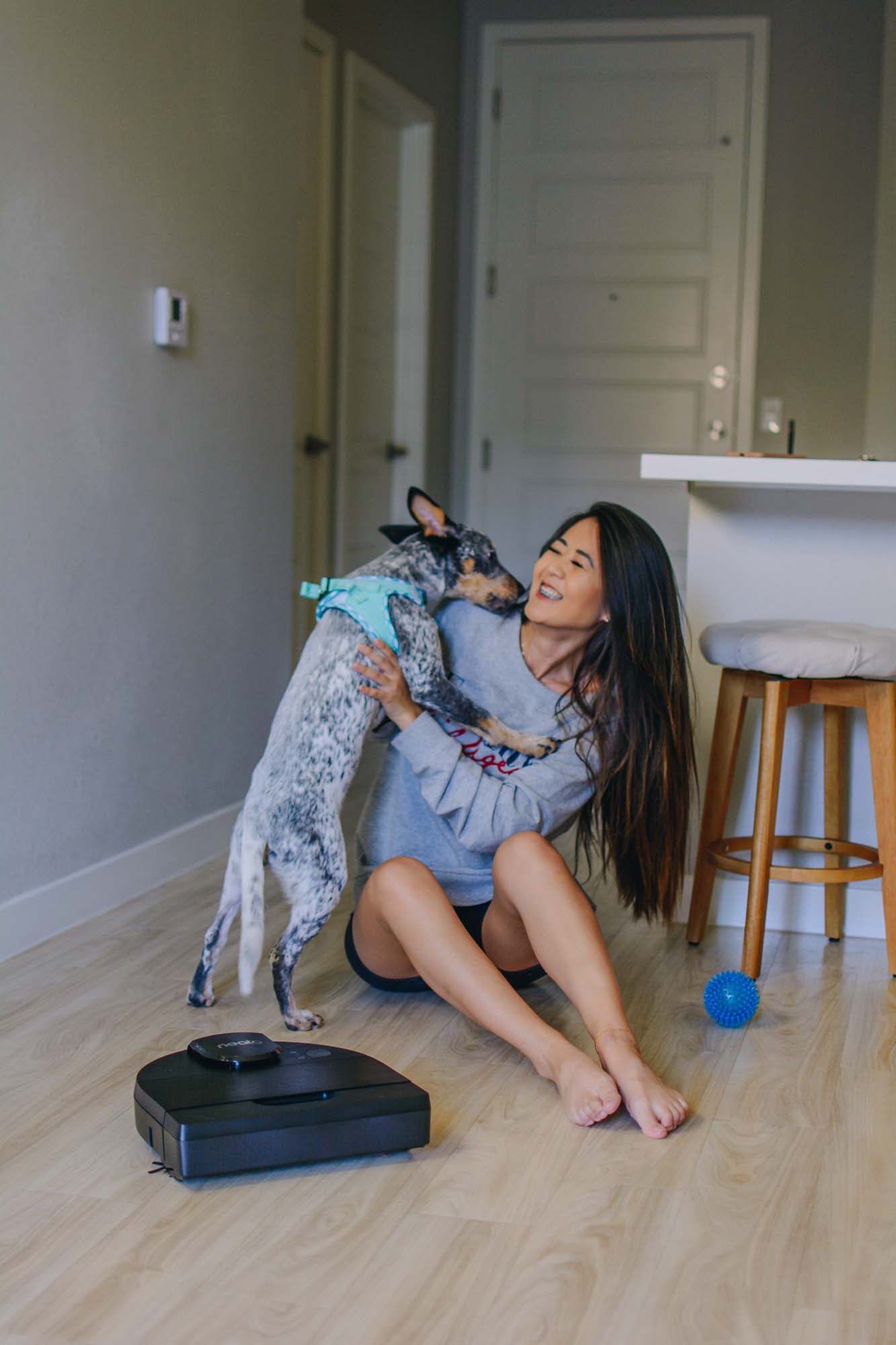Blogger Demi Bang playing with a dog while running an electric vacuum on her hardwood floors.